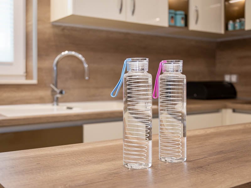Две стъклени бутилки Hygea Water със сребърни спирали вътре, върху кухненски плот